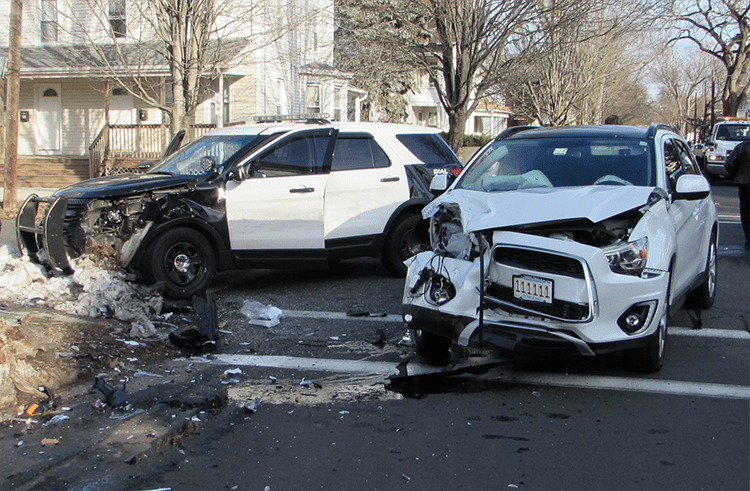 A damaged white SUV and a black-and-white police vehicle after a collision on a residential street. Debris is scattered on the road near the vehicles.