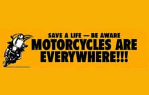Yellow sign with a motorcycle image and bold text: "SAVE A LIFE — BE AWARE MOTORCYCLES ARE EVERYWHERE!!!.