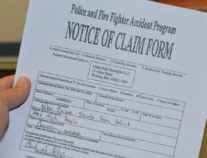 A person's hand holds a "Notice of Claim Form" from a Police and Fire Fighter Accident Program. The form includes handwritten details about an accident where a cruiser was struck from behind.