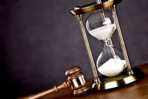 A wooden gavel lies next to a brass-framed hourglass with white sand on a wooden surface against a dark background.
