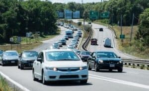 Traffic on a multi-lane highway with a mix of cars in both directions. Trees and road signs are visible in the background.