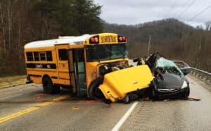 A school bus and a car collided head-on on a two-lane road. Emergency responders are on the scene.