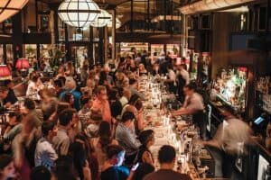 A crowded bar at night with people socializing and bartenders working behind the counter.