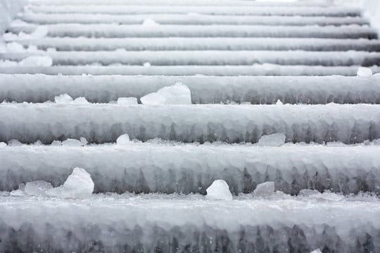 Close-up view of outdoor stairs covered in thick ice with scattered chunks of snow.