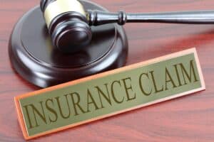 A wooden gavel and a nameplate reading "INSURANCE CLAIM" are placed on a polished wooden surface.