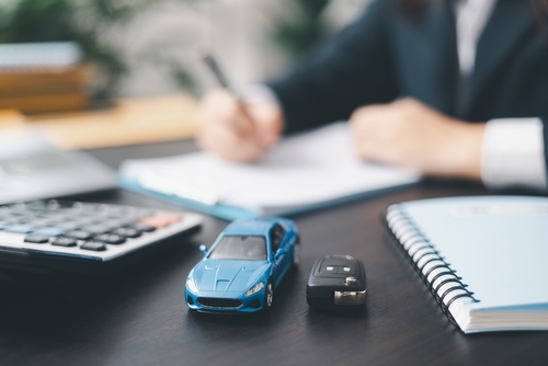 toy car and key on desk while person signs insurance document