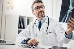 Doctor in lab coat examining x-ray film beside desk in medical office