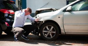 Man crouching beside damaged car after rear-end collision in parking area