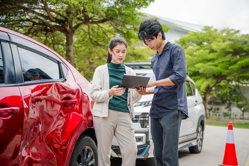 two people reviewing clipboard documents beside damaged vehicle at accident scene