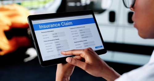 Person using tablet displaying Insurance Claim form beside damaged vehicle